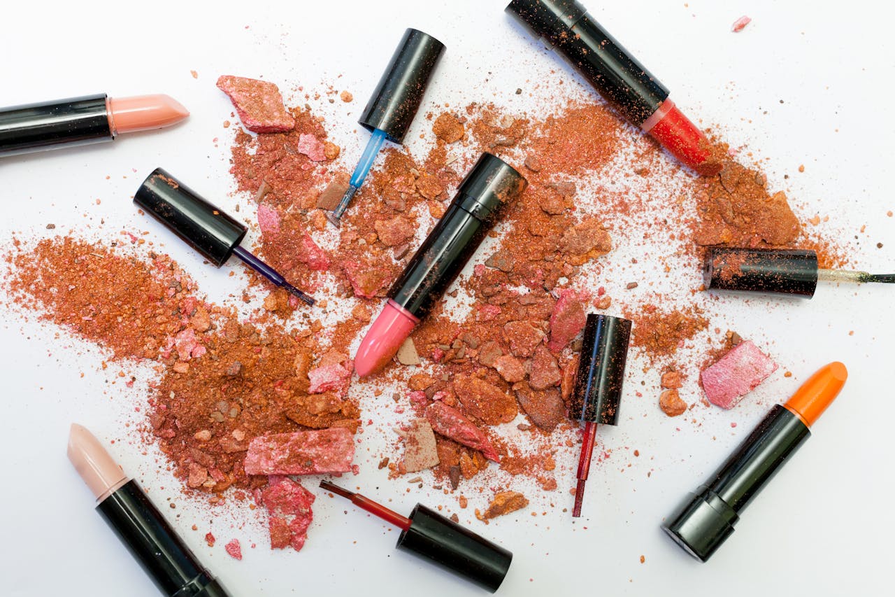gallery-4 Colorful scattered makeup products including lipsticks and crushed powders on a white background.
