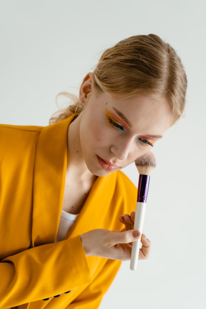 services-03 Close-up of a woman applying makeup with a brush, wearing bright yellow attire.