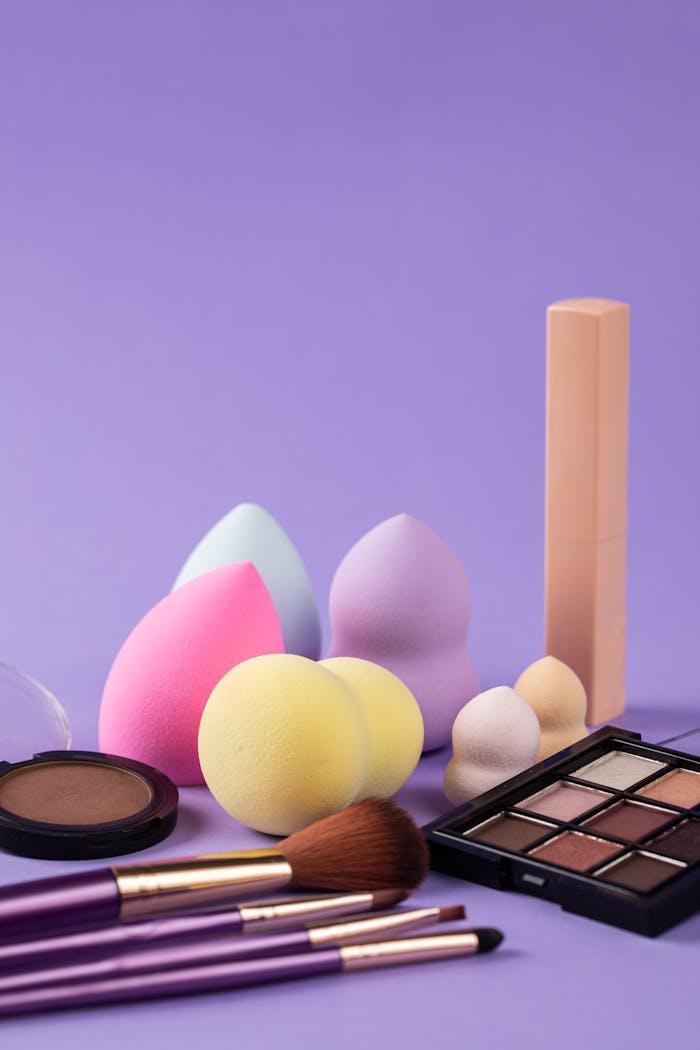 contact-img A collection of beauty blenders and makeup products on a purple background.